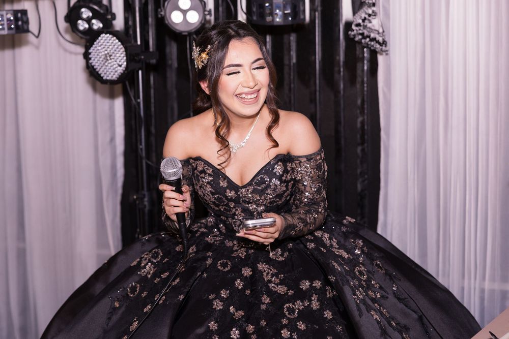 A person in a black floral dress laughs joyfully while posing against a dark background.