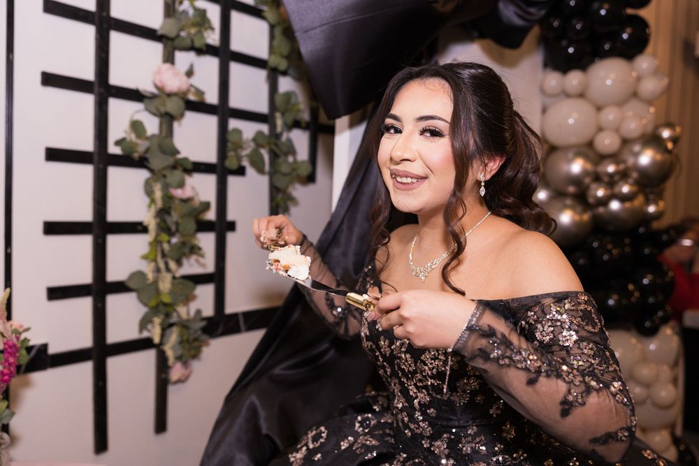 Elegant black lace gown with off-shoulder design photographed at festive party with balloons and string lights in background.