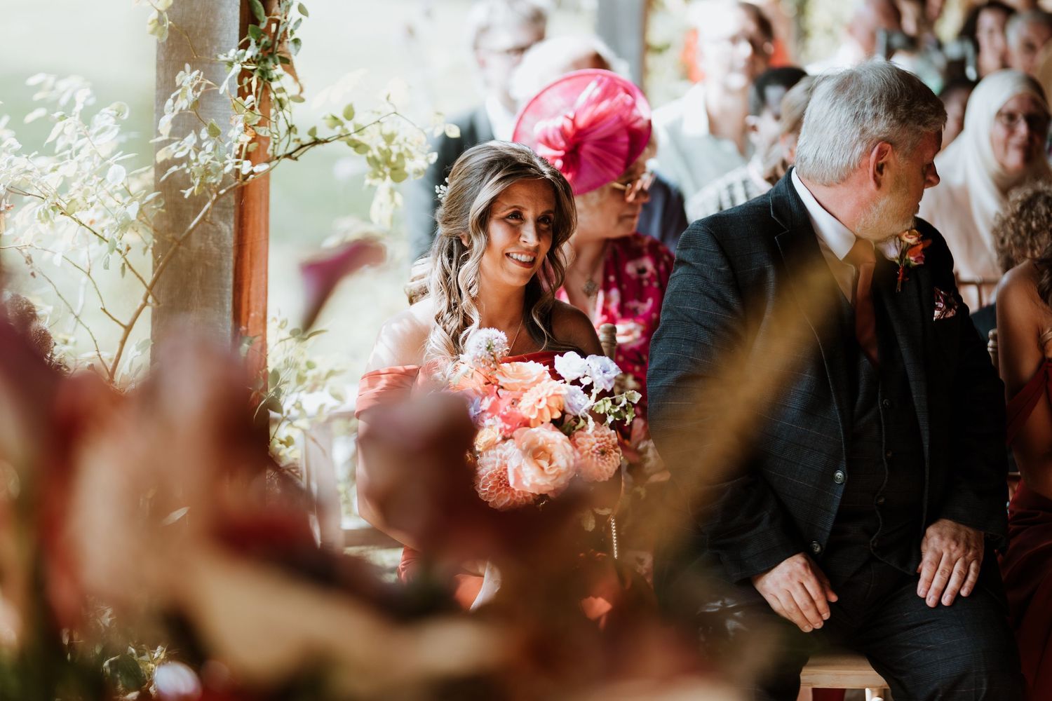 Wedding guests seated during an elegant ceremony with soft lighting and floral decorations in the background.