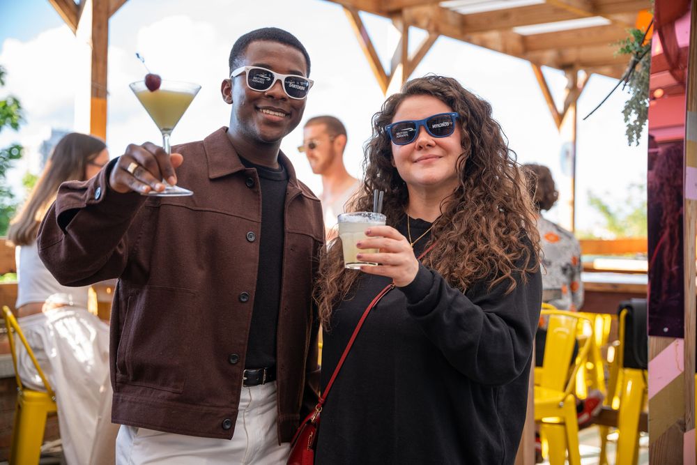 People socializing at an outdoor event under wooden pergola structure.