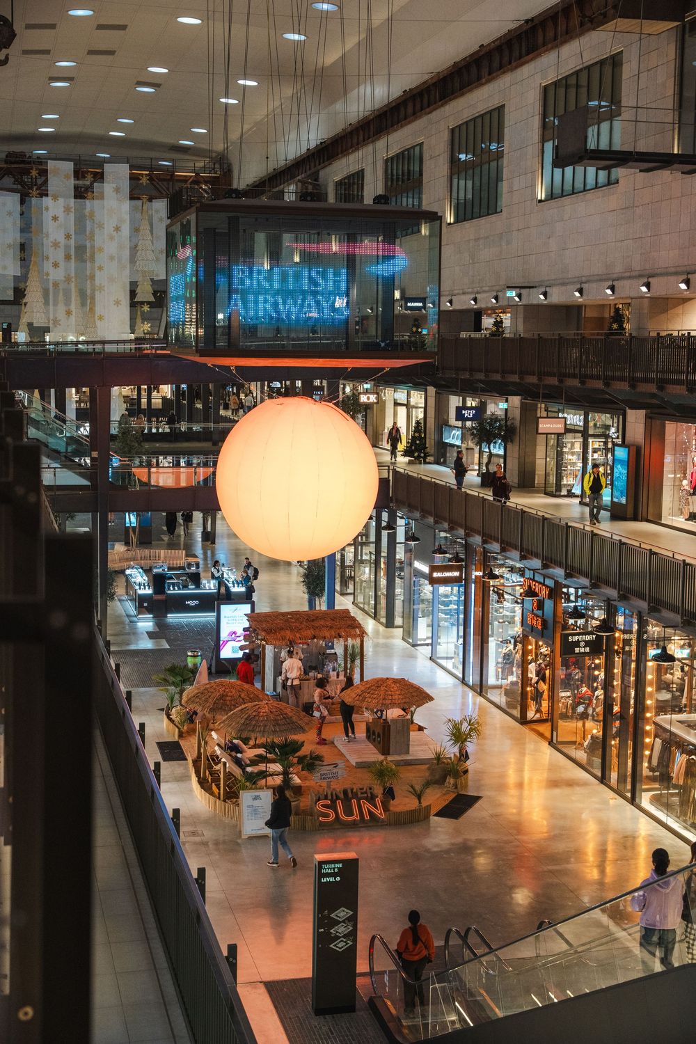 Modern shopping mall interior with British Airways signage and illuminated sphere decoration.