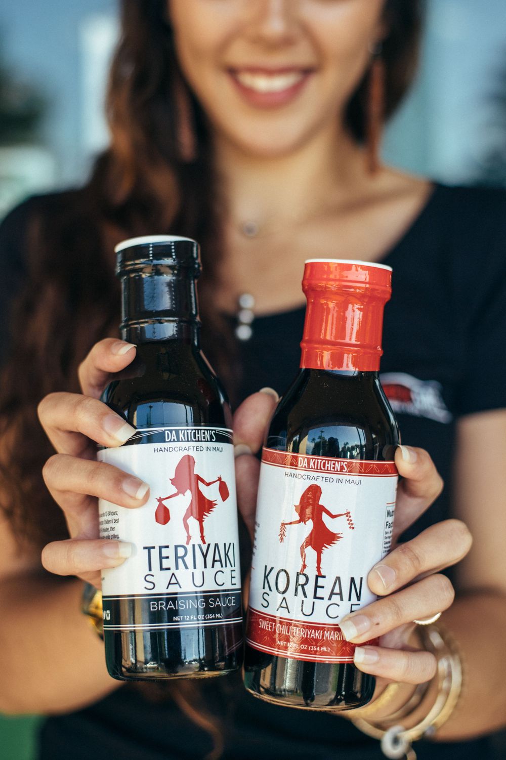 Close-up of hands holding teriyaki and Korean sauce bottles with red and black labels.