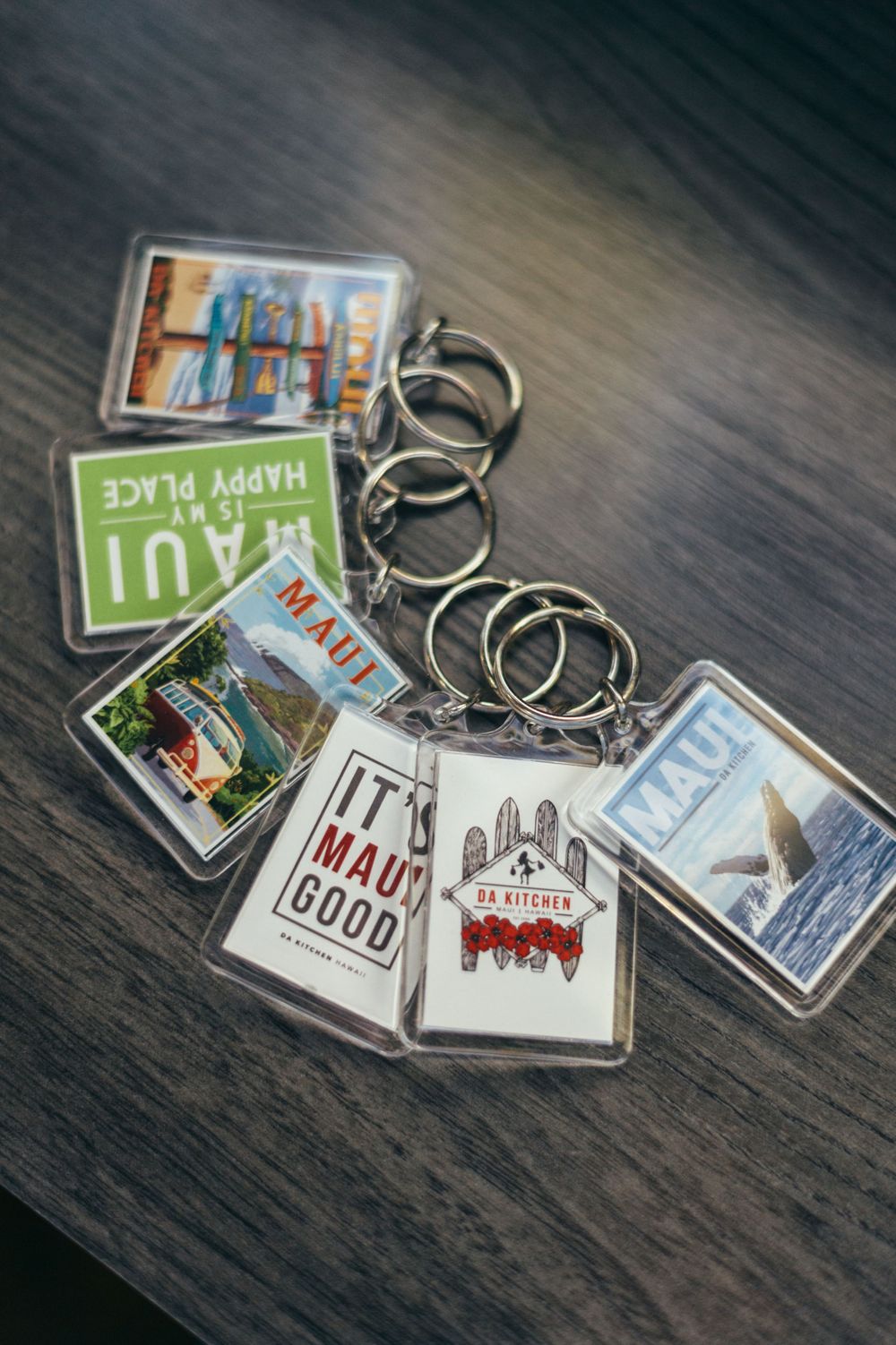 Collection of decorative keychains featuring Hawaiian-themed designs on dark wood surface.