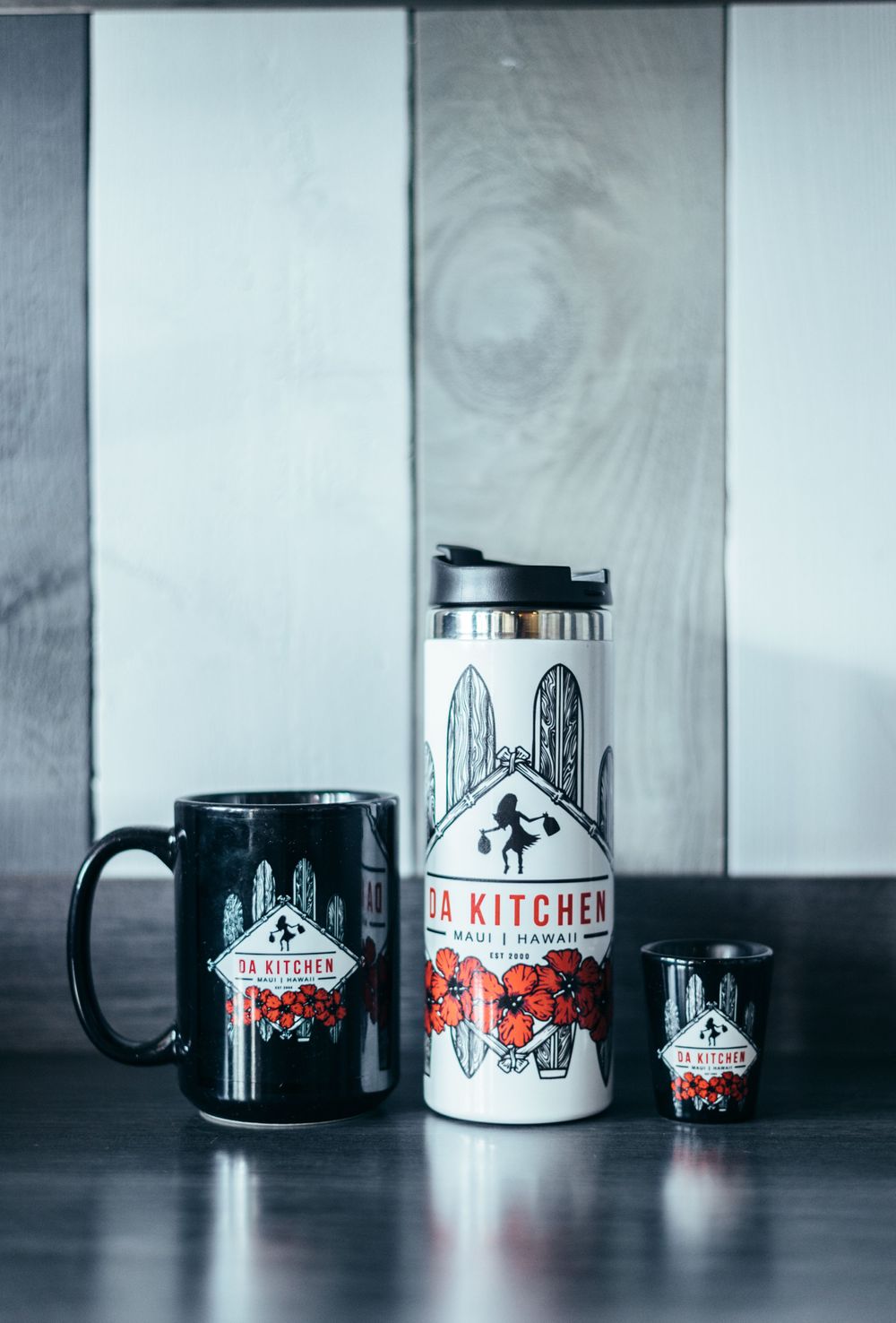 Collection of branded coffee mugs and tumblers with Da Kitchen logo in black and white.