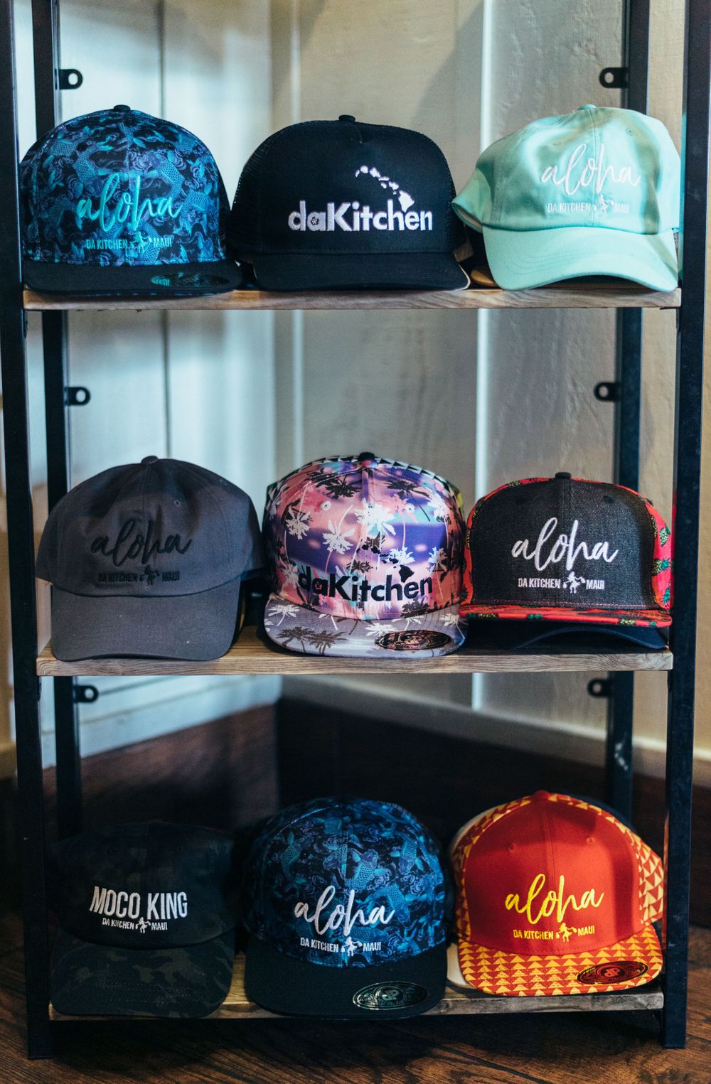 Display shelf showing various branded baseball caps with 'da Kitchen' and 'Aloha' designs.
