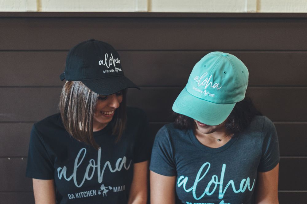 Two people wearing matching Aloha branded t-shirts and baseball caps.