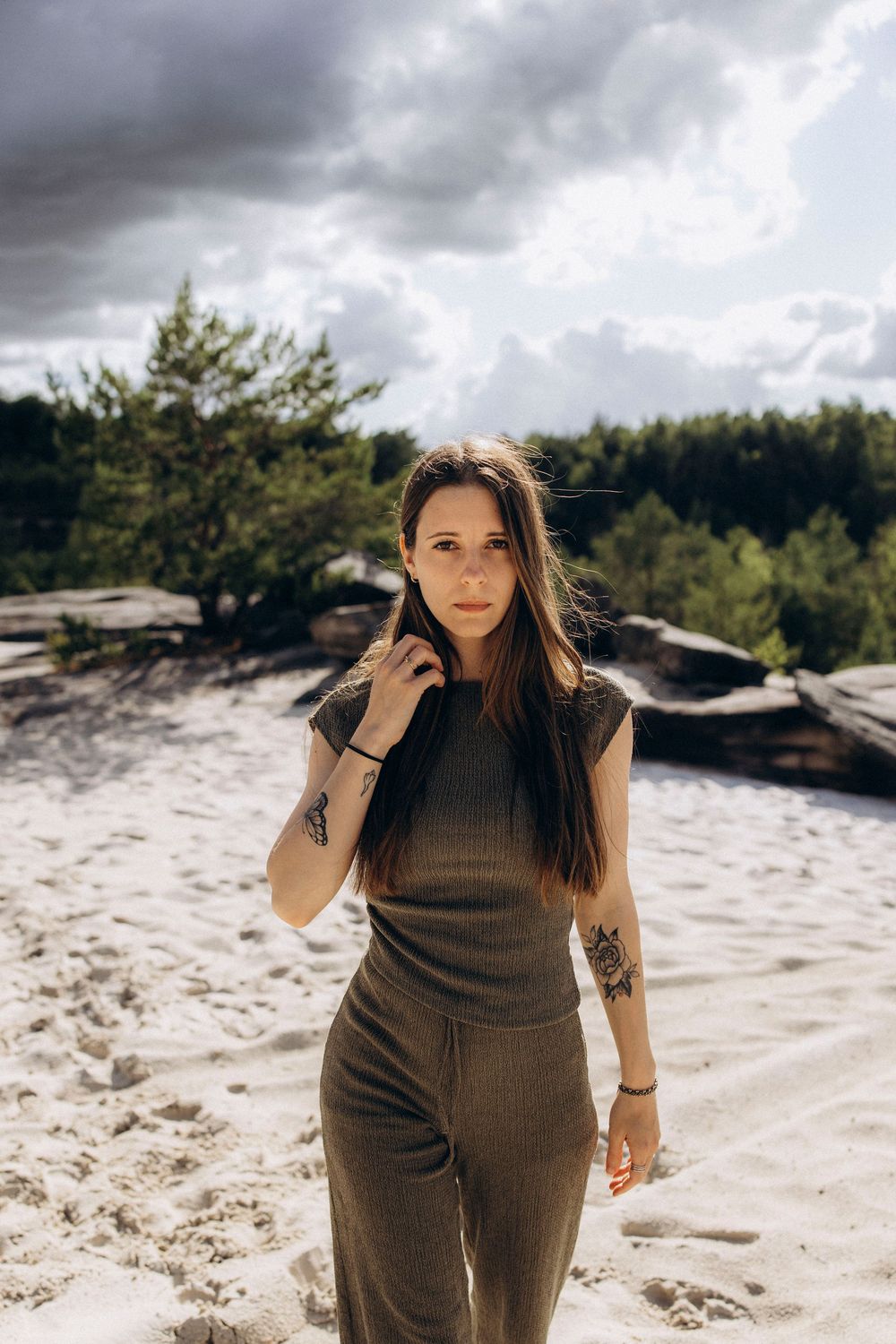 A sequence of photos showing someone in a brown outfit posing on a sandy beach with dramatic cloudy skies.