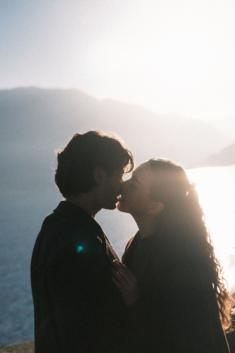 Silhouetted couple embracing against bright sunlit sky in romantic backlit series of photos.