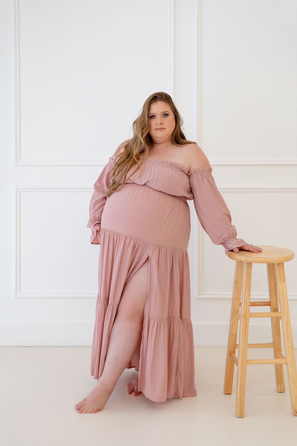 A soft pink off-shoulder maxi dress is displayed in multiple angles against a white backdrop with wooden stools.