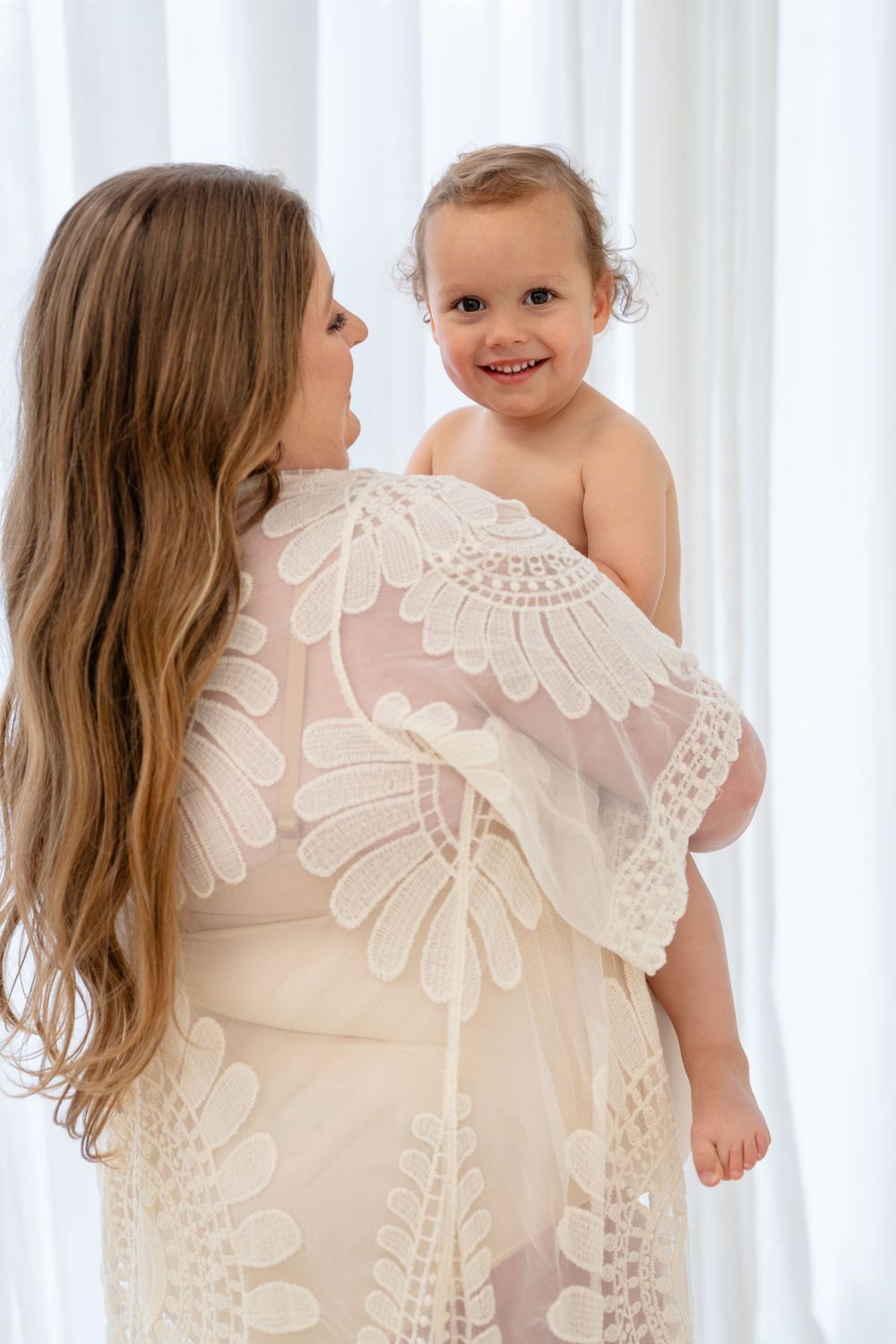 A tender moment between parent and child wearing a white lace dress against a bright backdrop.