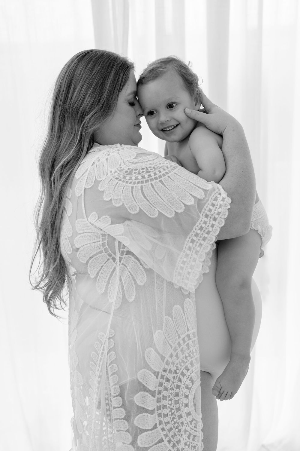 Mother and child share intimate black and white portrait moments against white backdrop.