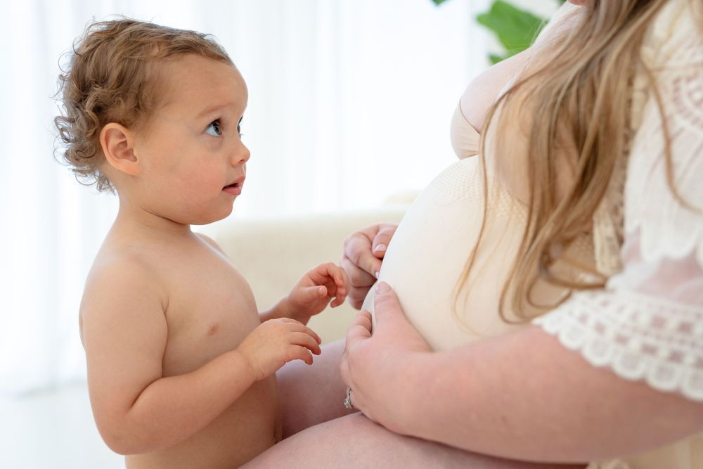 A mother breastfeeding her infant child while sitting in a bright, sunlit room.