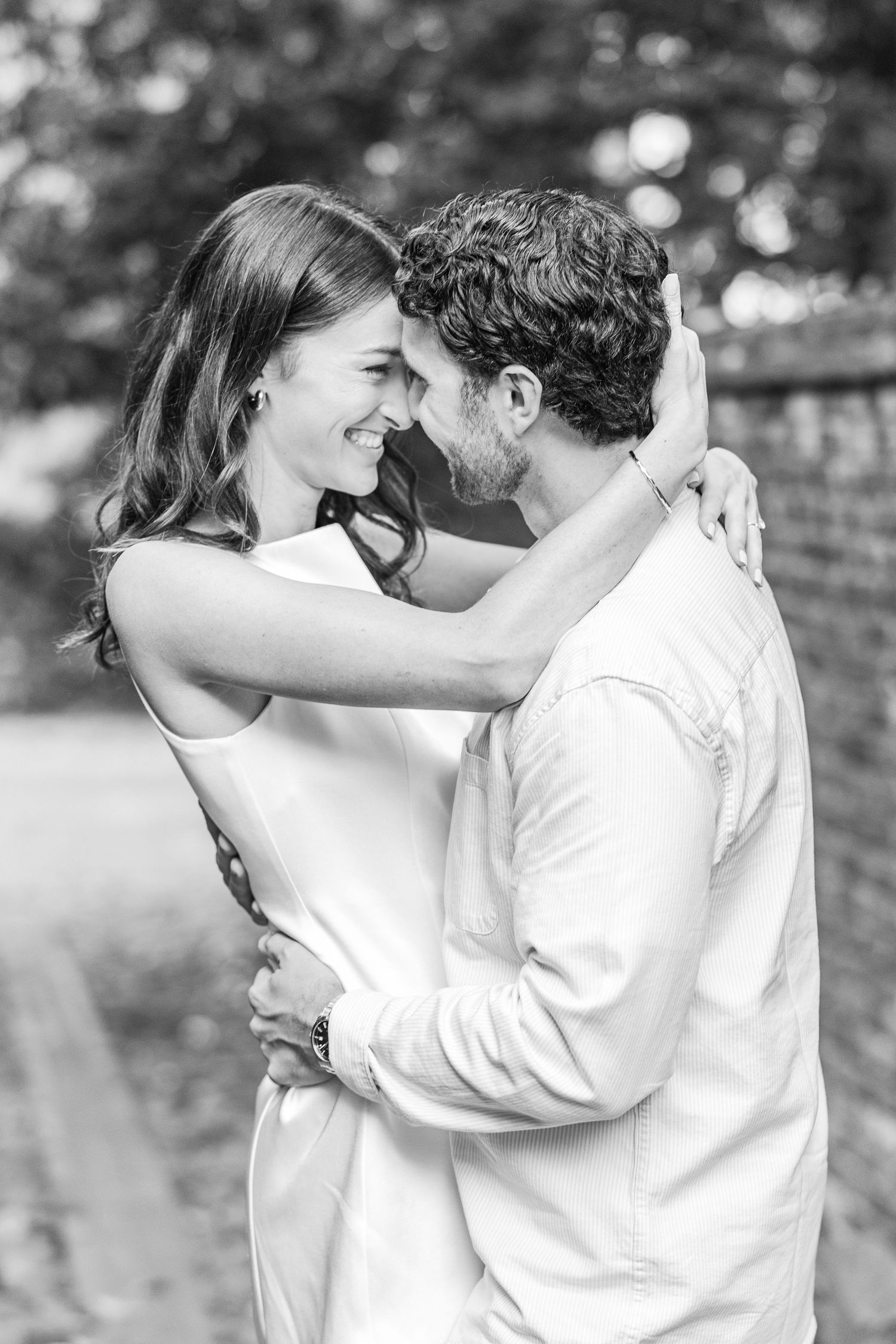 A romantic black and white portrait of a couple embracing and laughing together outdoors.
