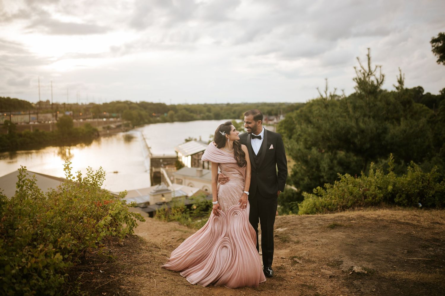 A romantic sunset wedding photoshoot with a couple in formal attire walking through a scenic outdoor landscape.