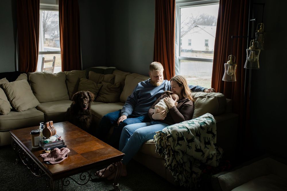 A dimly lit living room shows someone resting on a couch while natural light streams through the windows.
