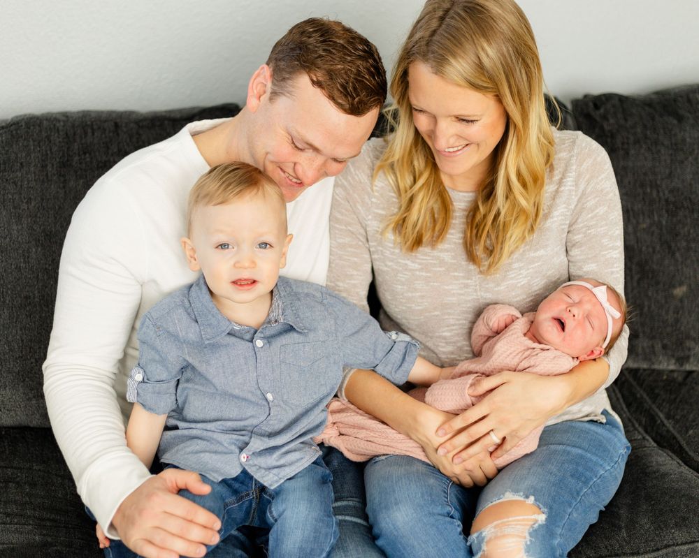 Family relaxing together on grey couch in casual attire.