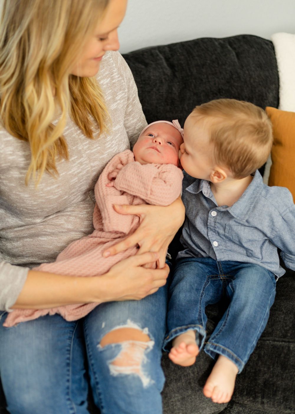 Tender family moment on dark couch with casual denim and grey clothing.