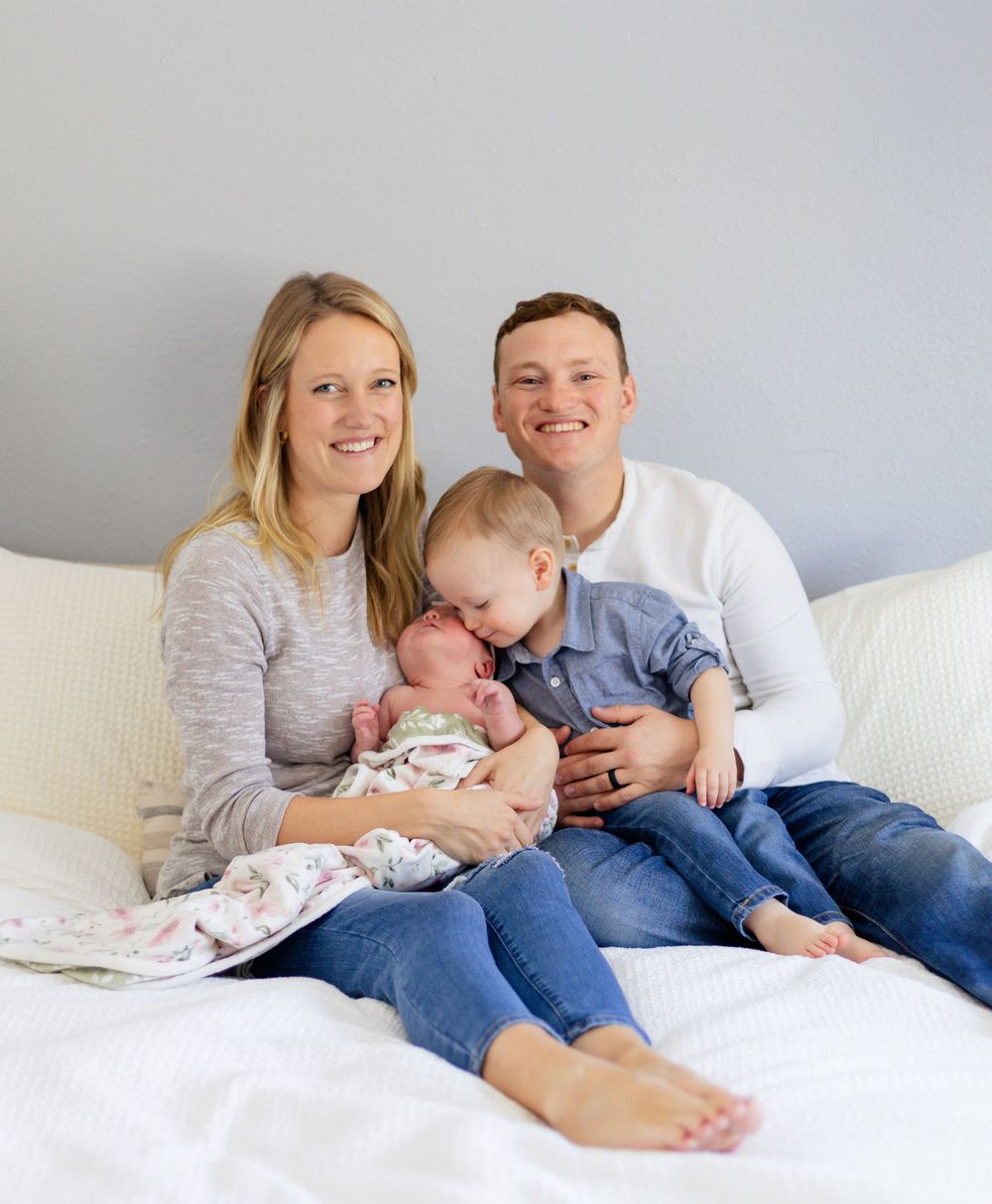 Family lounging together on white couch with small baby in casual attire.