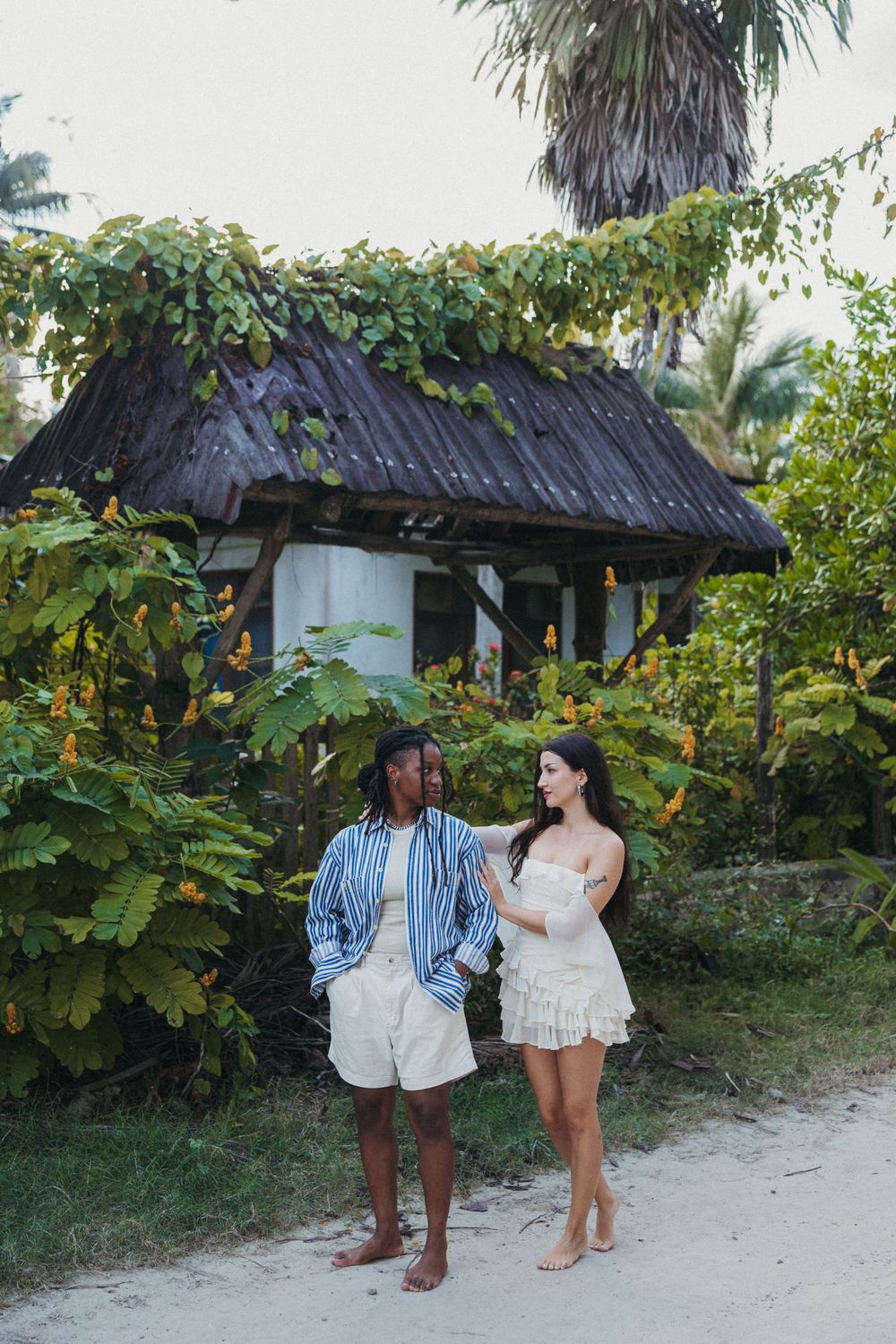 Couple sharing a tender moment on a sandy beach path with tropical foliage and a thatched hut in the background at Holbox