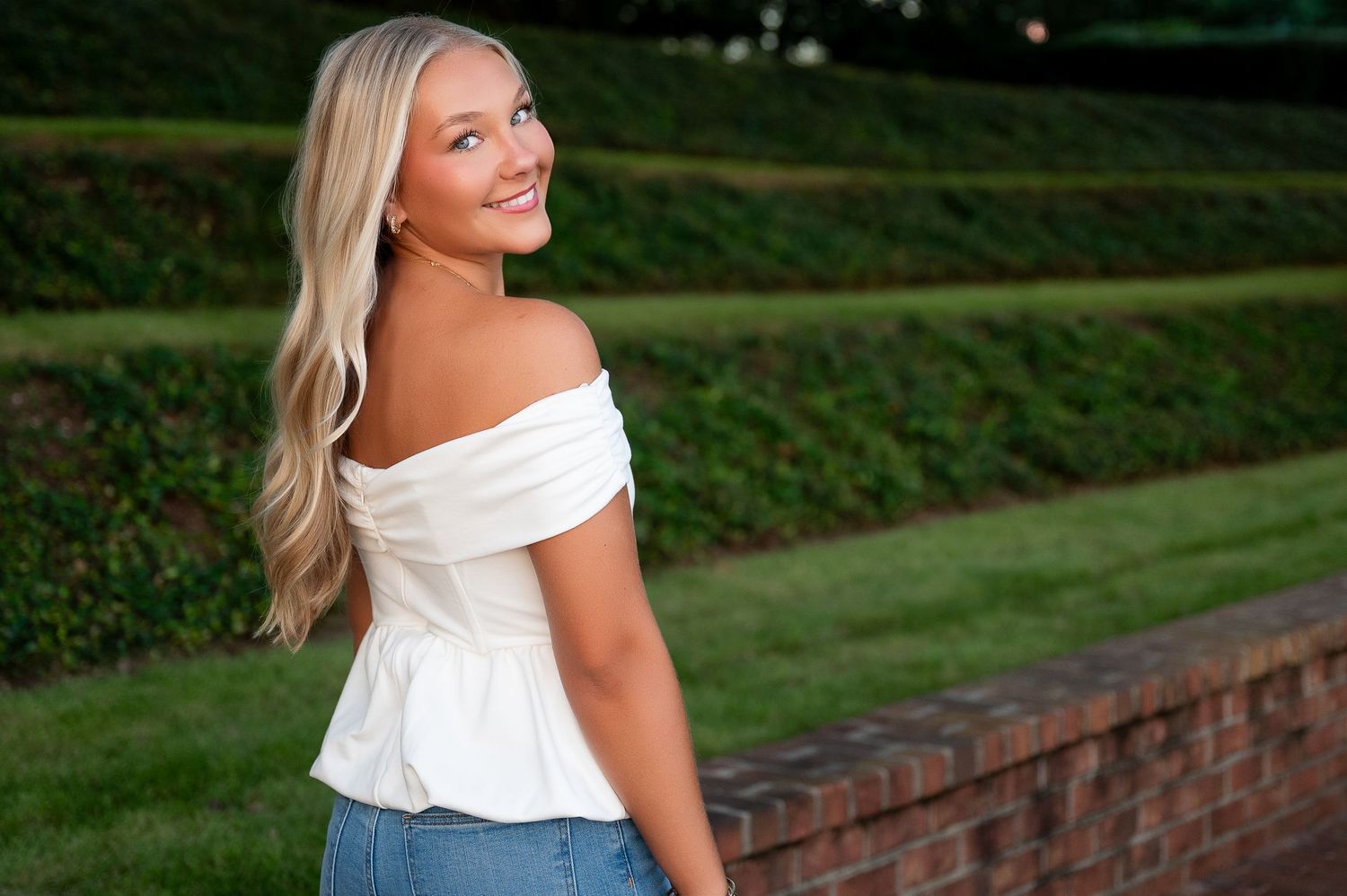 White off-shoulder top styled against green garden background.