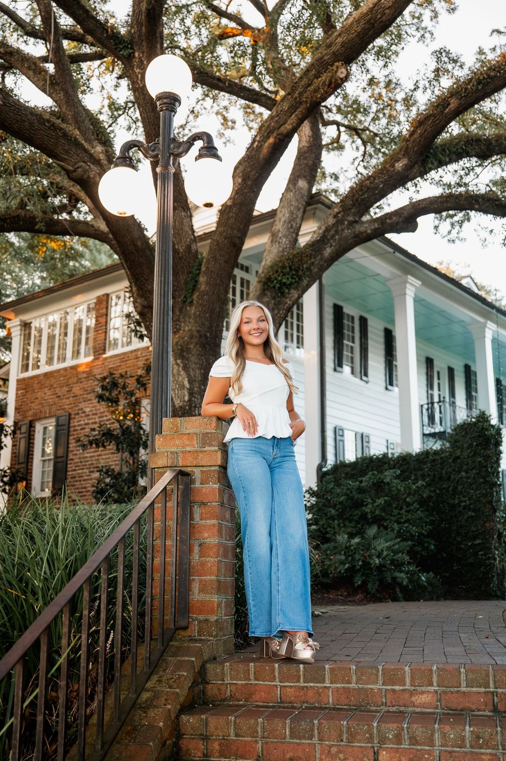 White top and jeans outfit photographed near historic house with wraparound porch.