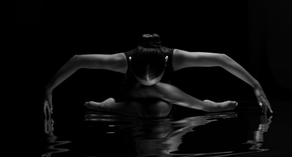 A silhouetted figure performs an elegant ballet pose against a dark background creating a dramatic artistic effect.