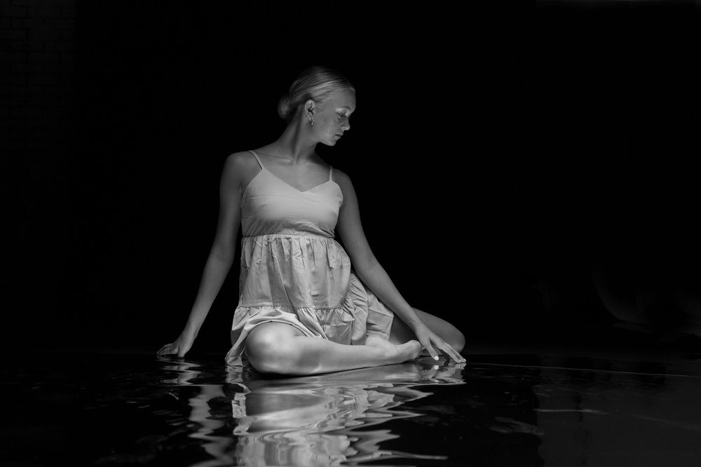 A person in a white dress sits in dark water creating an artistic underwater portrait series.