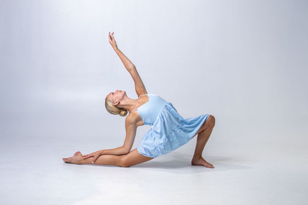Dancer in light blue dress performs graceful movement sequence against white background.
