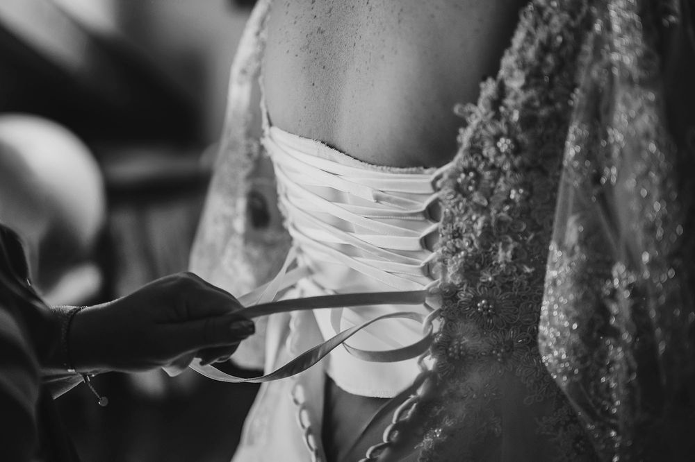 Primo piano in bianco e nero di mani che allacciano un abito da sposa in stile corsetto.