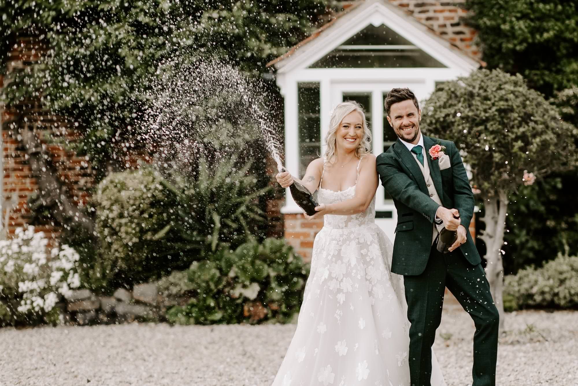 A romantic wedding couple shares joyful moments together in a garden setting with brick walls and lush greenery.