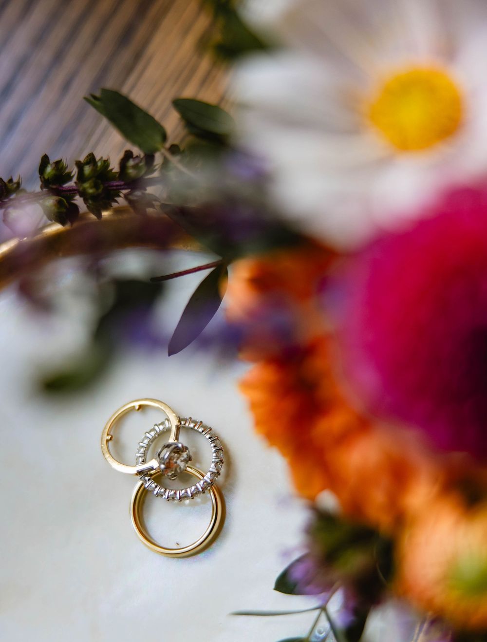 Gold wedding rings photographed with soft focus floral elements in the background. Appleford Estate. Villanova, PA.