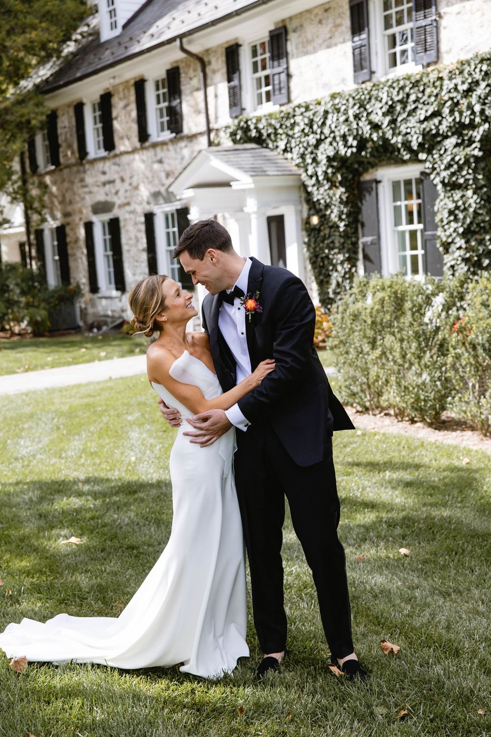 Newlyweds share intimate moments in front of a beautiful white stone house with climbing vines. Appleford Estate. Villanova, PA.