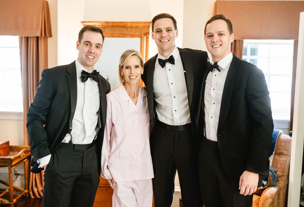 Wedding party members in formal attire posing together in a sunlit room. Appleford Estate. Villanova, PA.