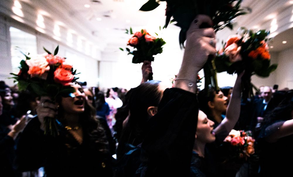 A dark silhouetted crowd gathers in front of bright white lights at an indoor event or concert venue.