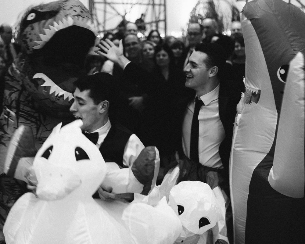 A group of people dancing and celebrating at what appears to be a wedding reception in black and white.