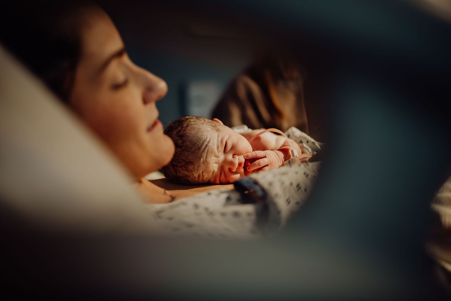 A sleeping newborn baby swaddled in white fabric rests peacefully in soft lighting.