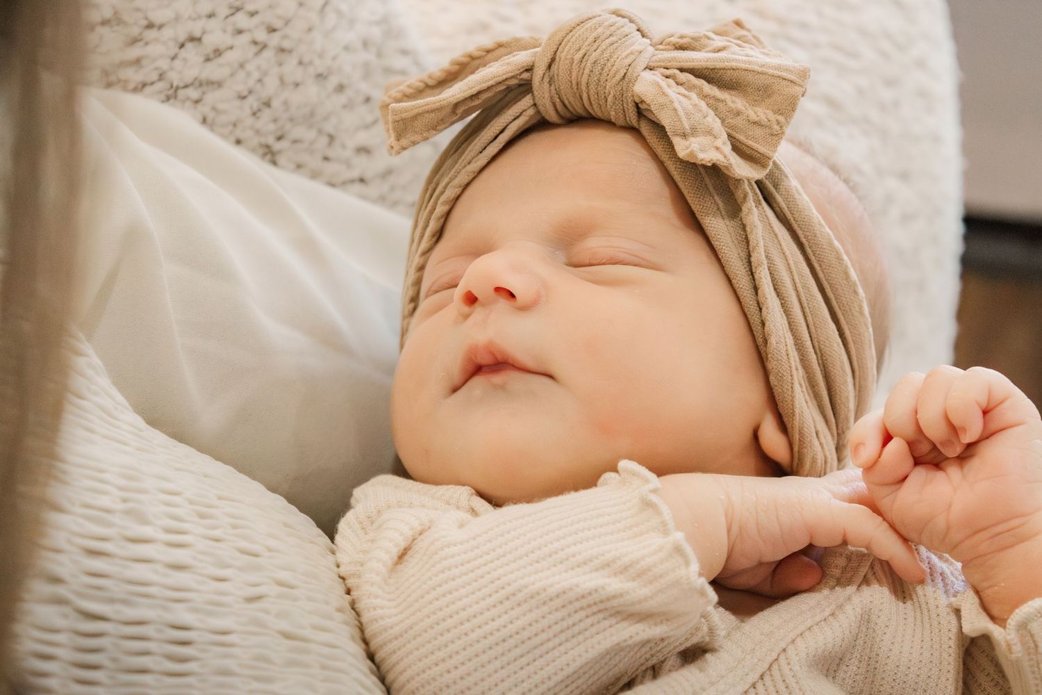 A sleeping baby lies peacefully in a white woven bassinet with a cozy knit blanket.