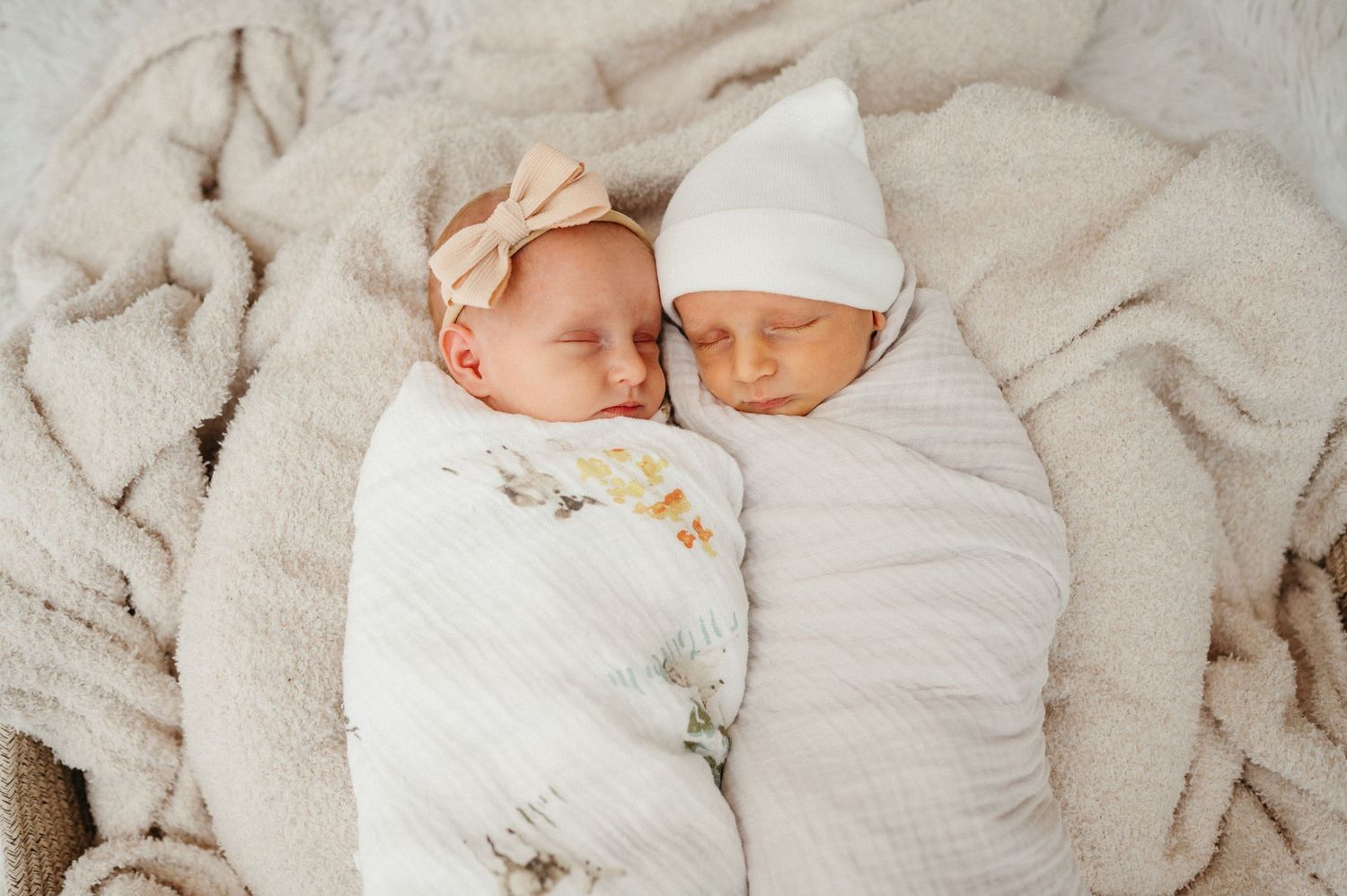 Two sleeping newborns swaddled side by side in white wraps.