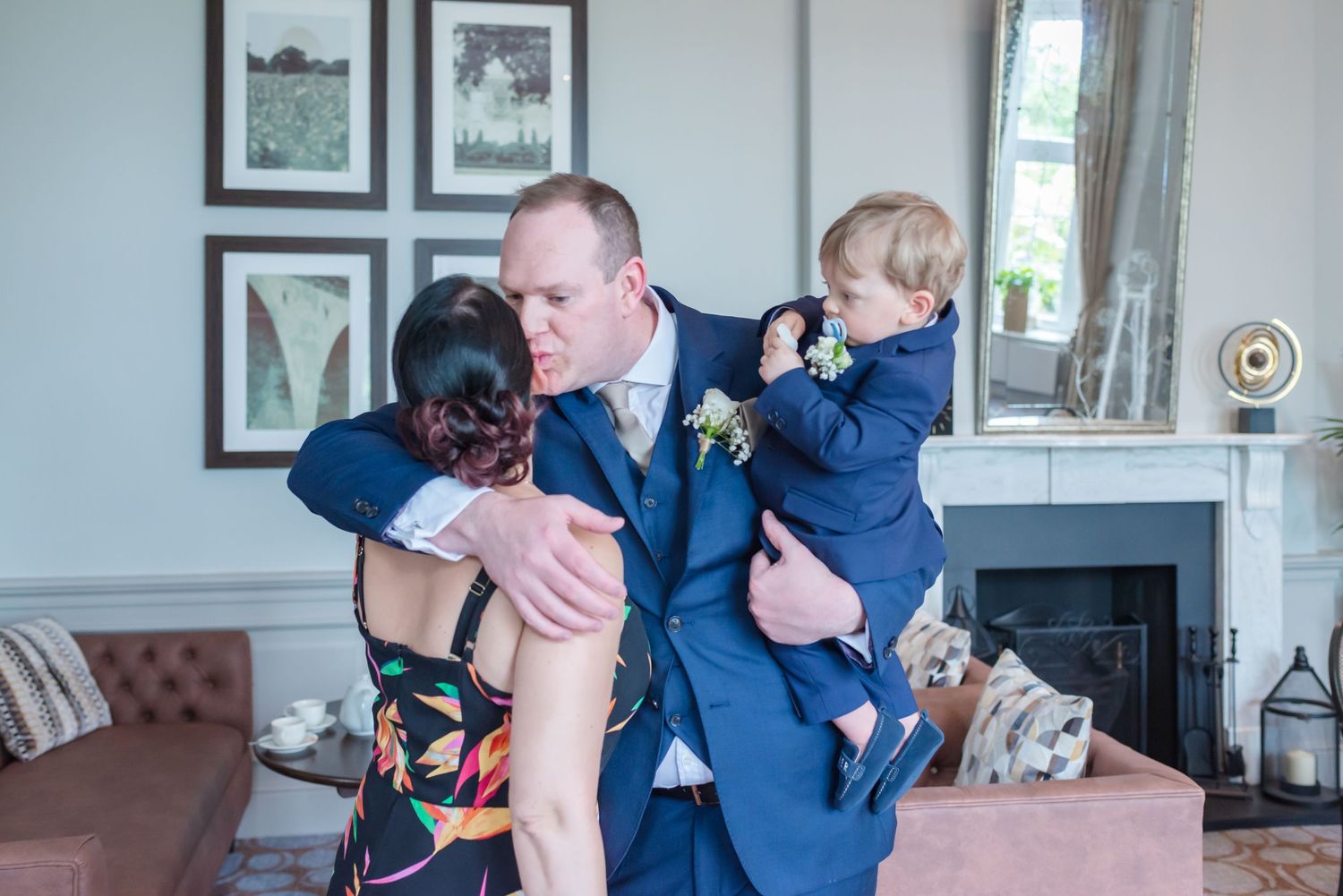A wedding party celebrates with joyful hugs and embraces while wearing navy blue attire at DeVere Cranage Estate in Cheshire