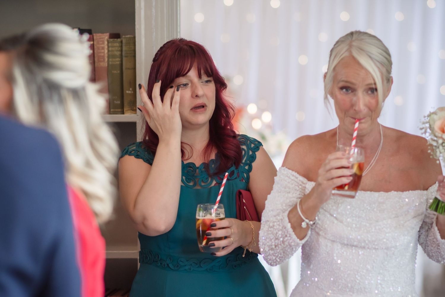 People enjoying drinks and conversation at a wedding reception with a person in emerald green dress and white bridal gown.