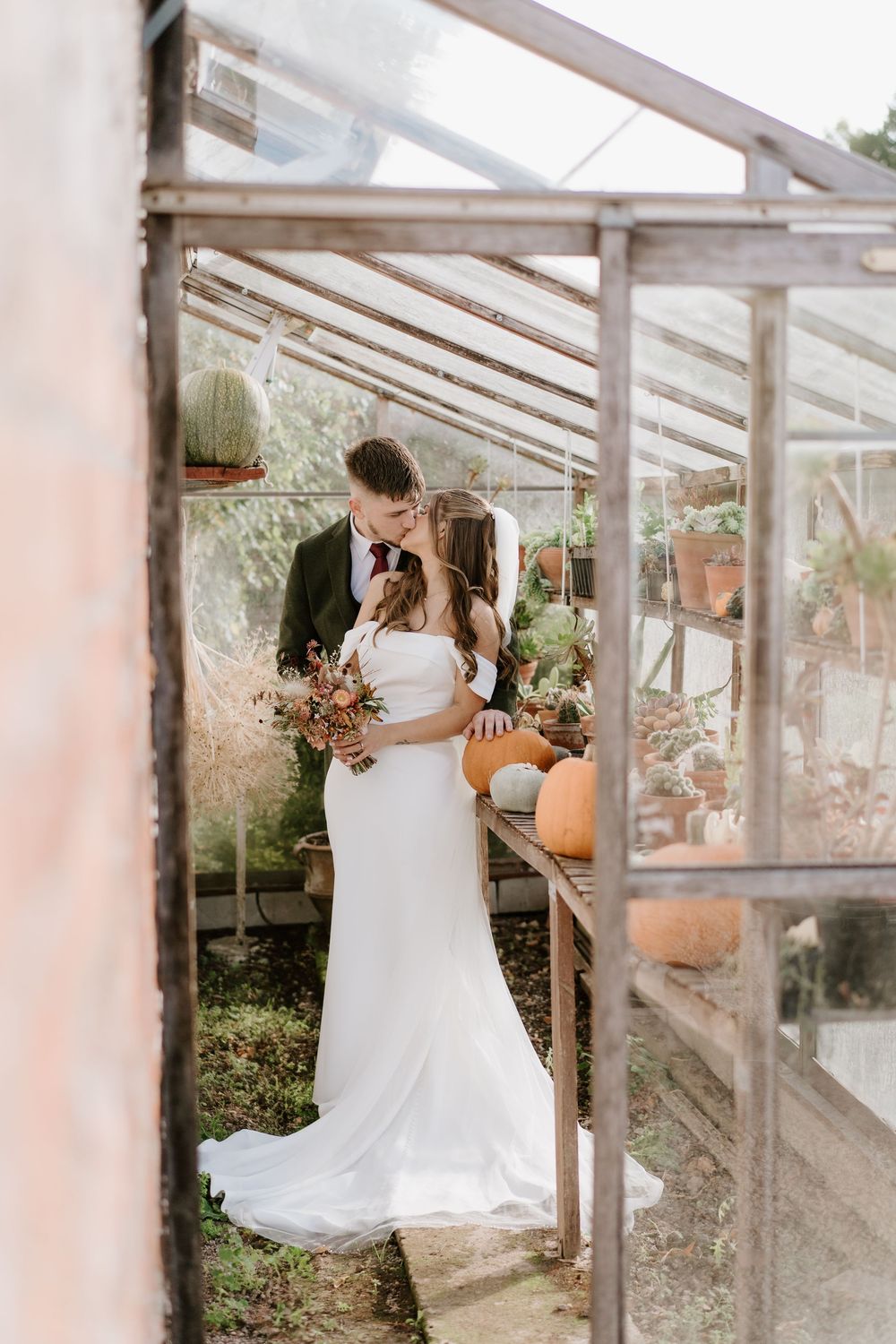 A romantic wedding moment captured in a rustic greenhouse with autumn pumpkins and floral arrangements in the Cotswolds.