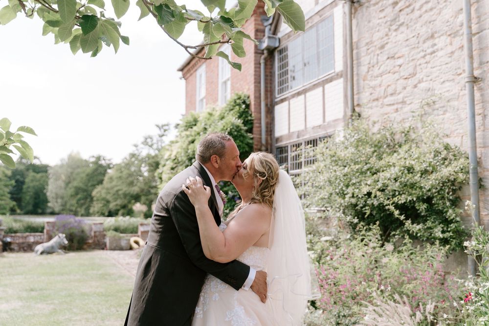 A couple shares an intimate dance moment in a garden setting with stone buildings in the background.