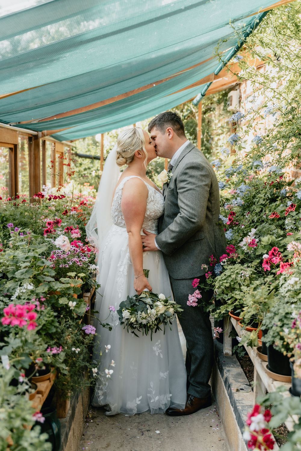 A romantic wedding moment unfolds in a greenhouse surrounded by vibrant pink flowers and lush greenery at Worcestershire Wedding Venue