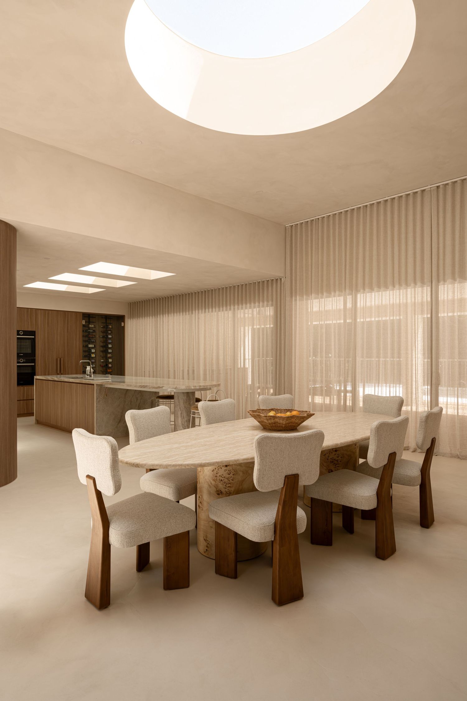 Modern dining room with oval white table, upholstered chairs, wooden accents and sheer curtains in neutral tones.