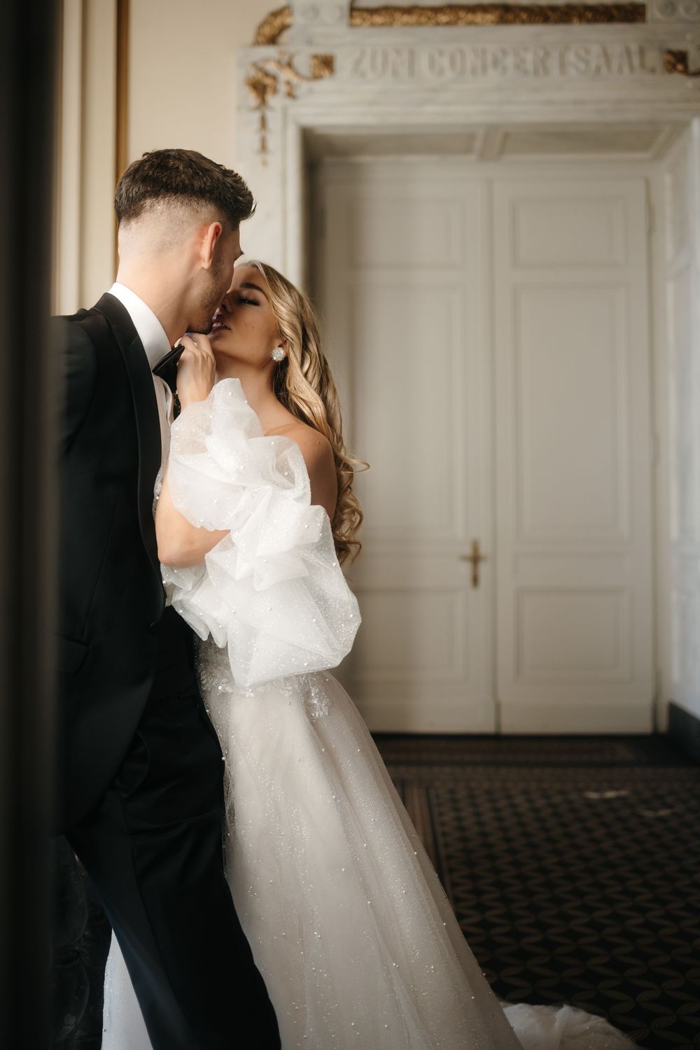 Romantic wedding couple embracing in an elegant white interior setting.