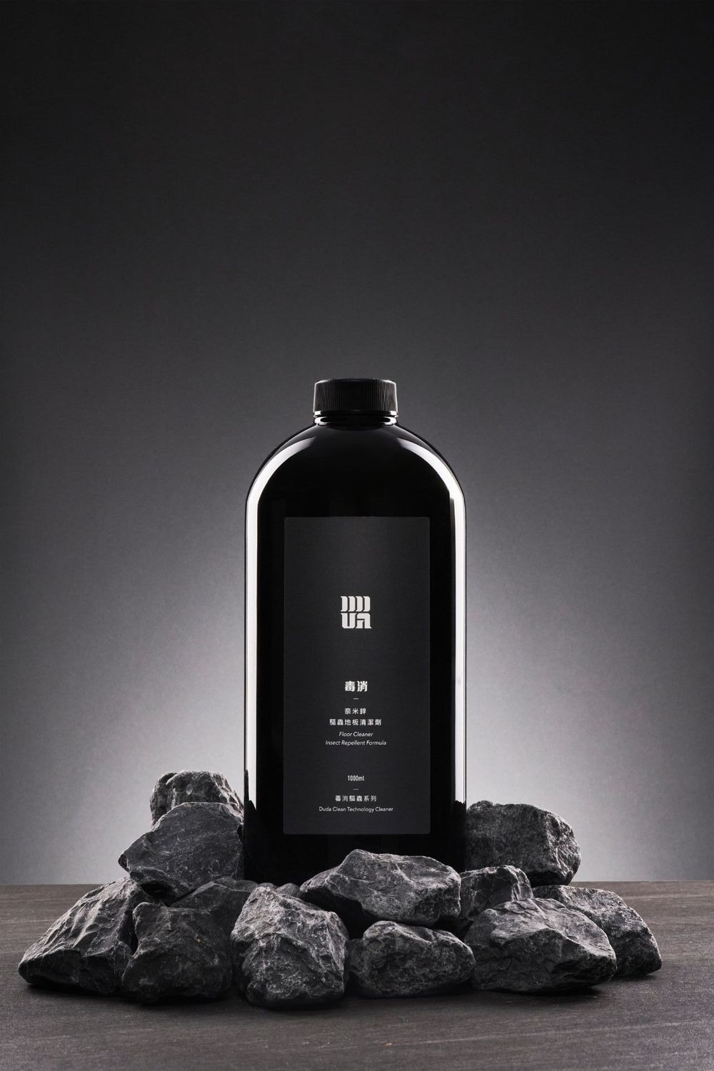 Black minimalist product bottles displayed on dark rocks against dramatic lighting in a luxury product photography series.