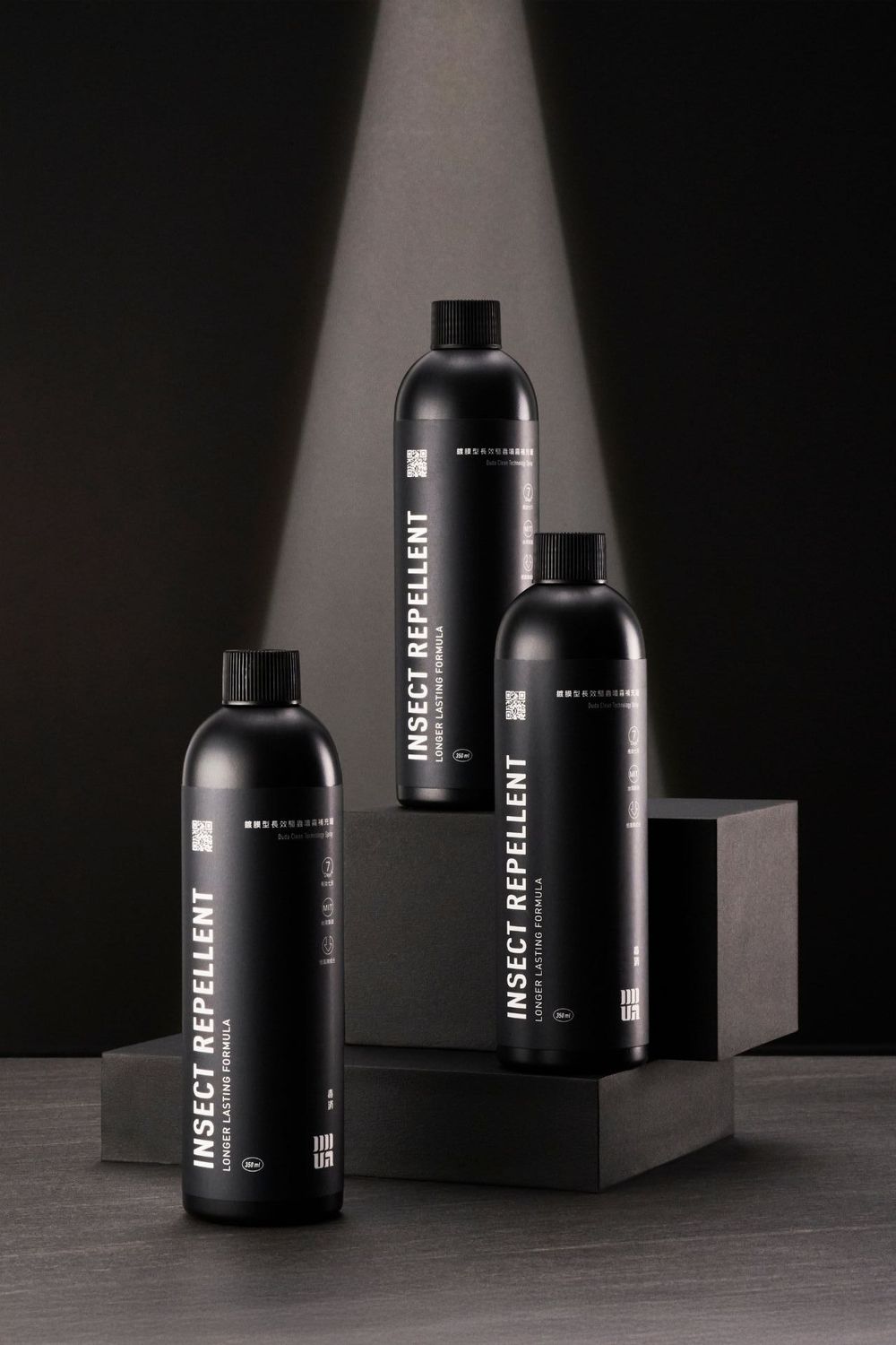 Minimalist black cosmetic bottles and packaging arranged in dramatic lighting against dark background.