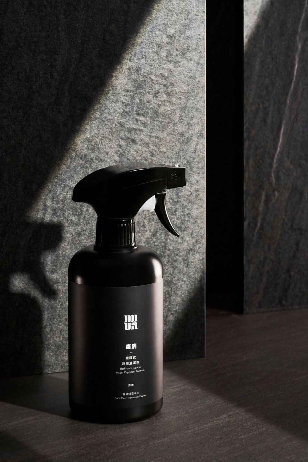 A sleek black spray bottle photographed in dramatic lighting against a textured dark background creates a moody product shot.