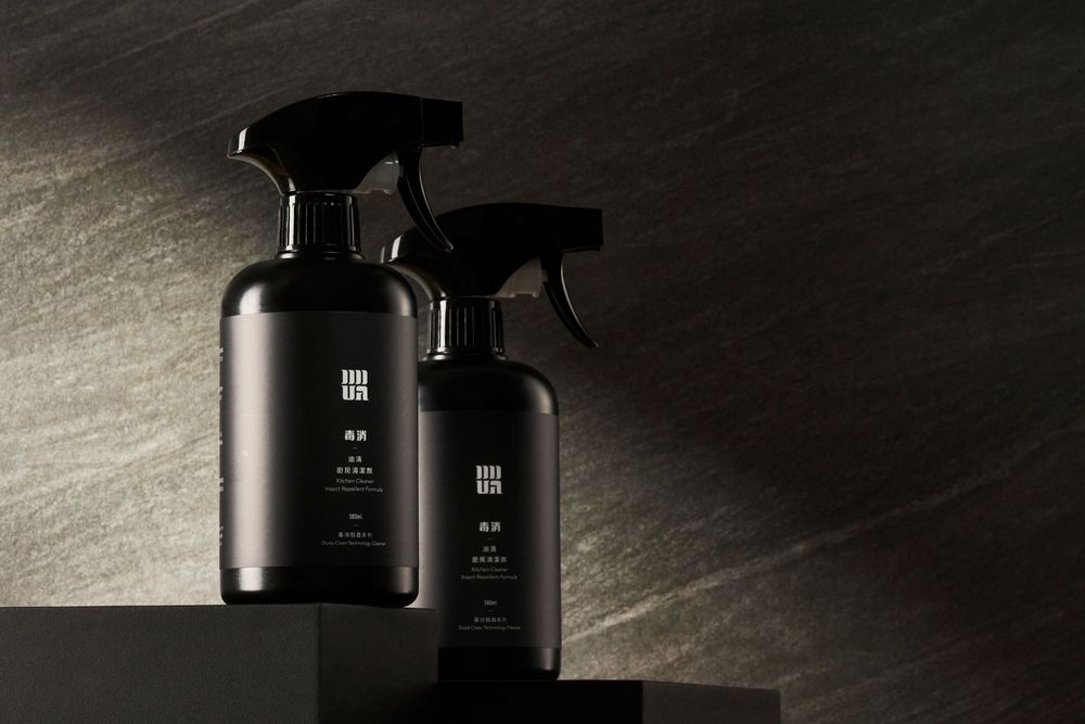 Two black spray bottles with minimalist design stand against a dark background with dramatic side lighting.