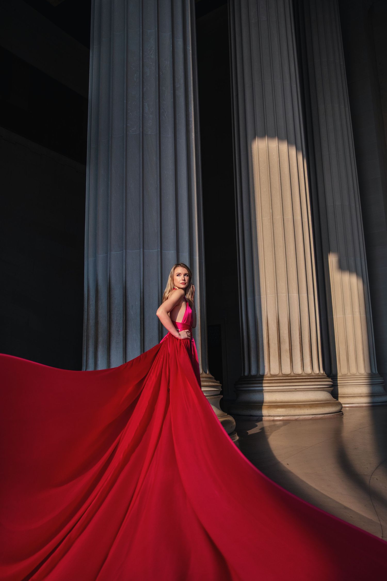 A flowing red gown dramatically sweeps across a columned backdrop in a series of elegant fashion photos. Washington DC Cherry Blossom
